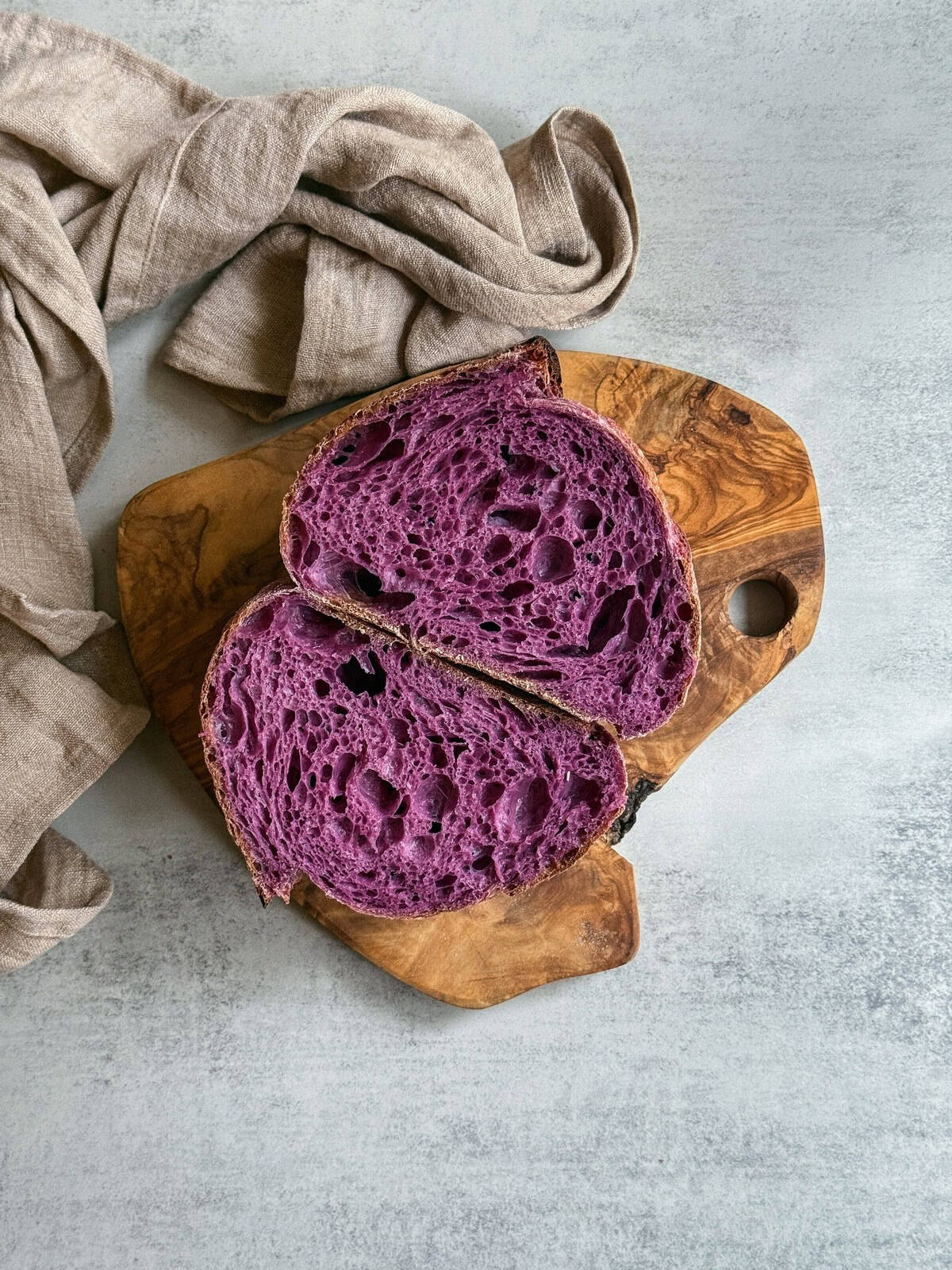 Purple sweet potato sourdough bread sliced in half on a wooden board.