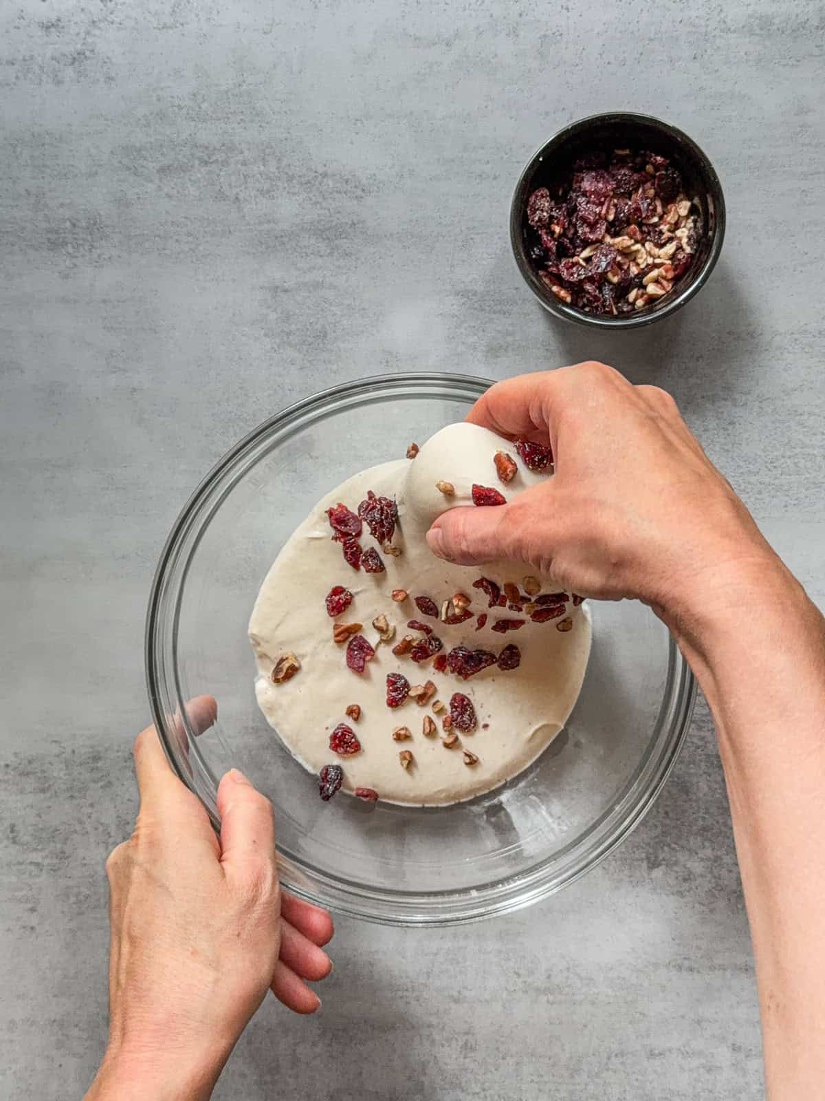 Dough with inclusions being stretched by hand over a glass mixing bowl.