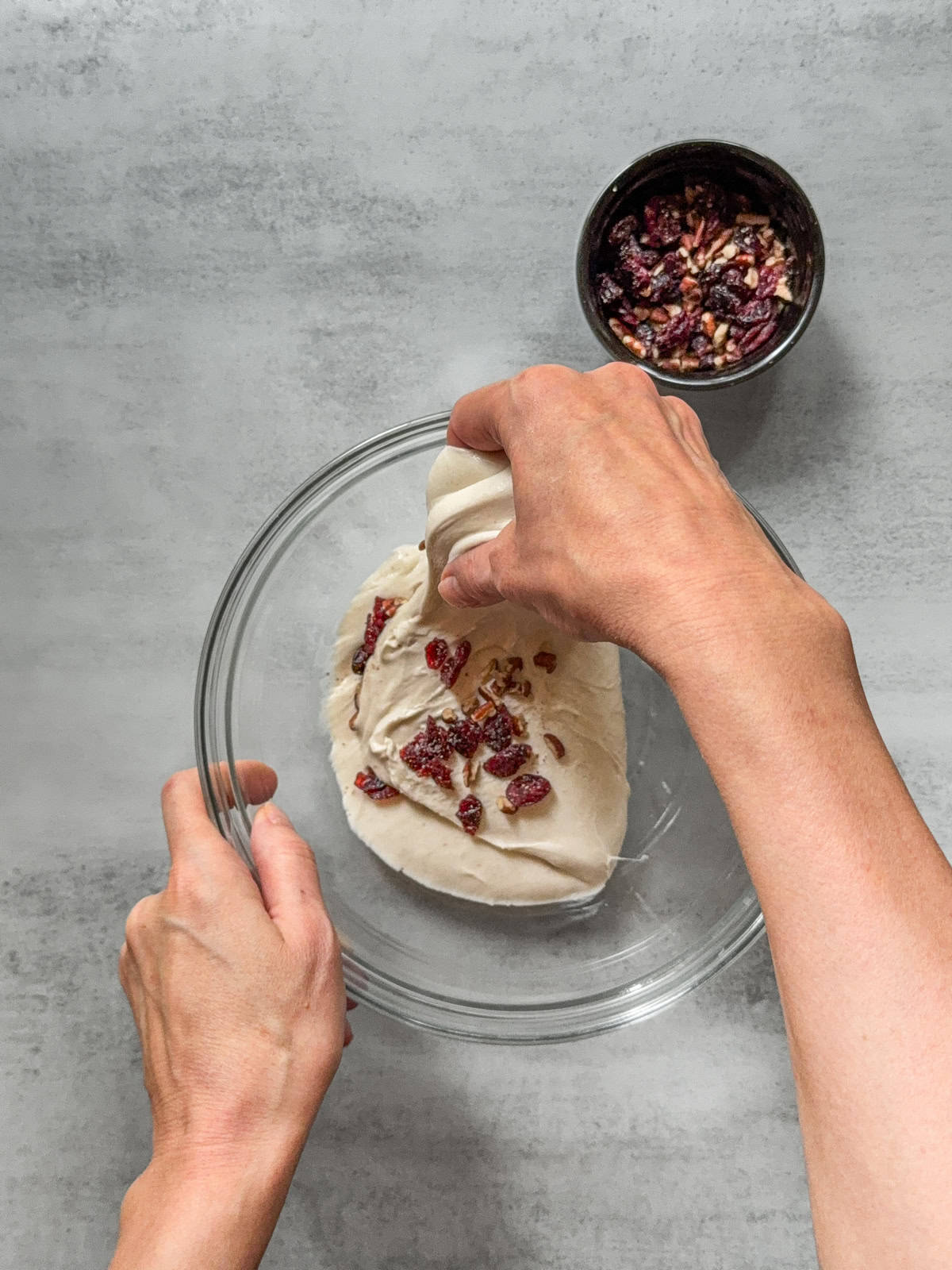 Hand stretching dough with inclusions over a glass mixing bowl.