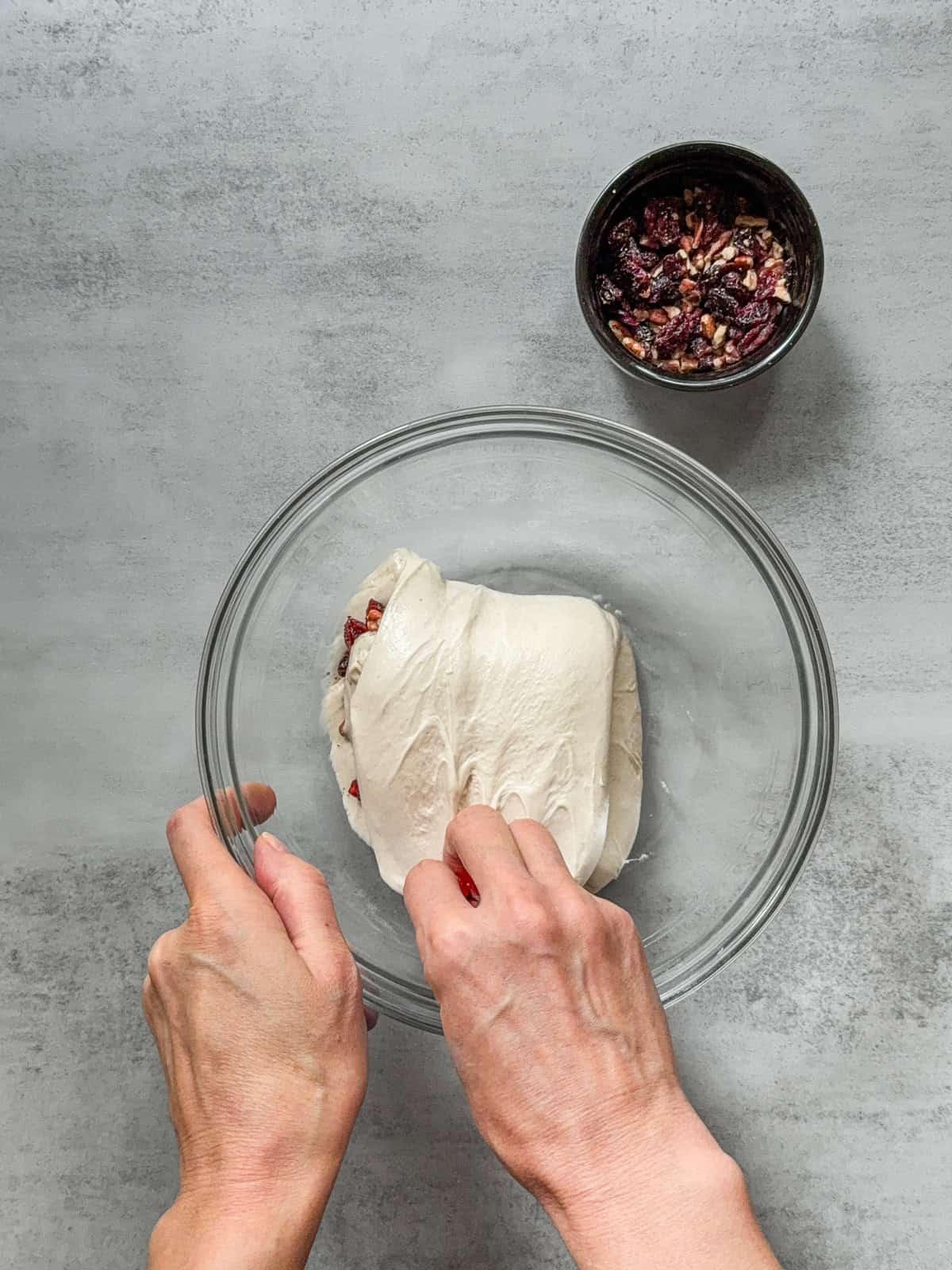 Hand folding stretched dough with inclusions in a mixing bowl.