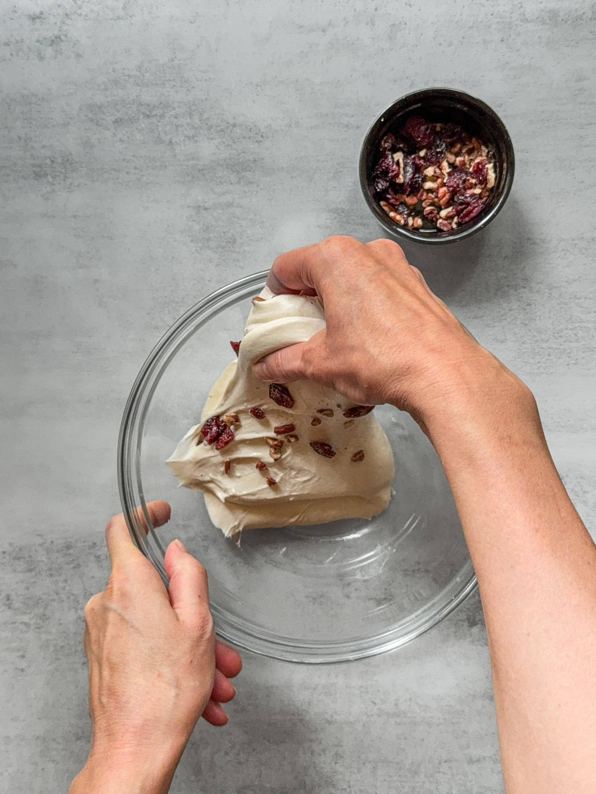 Stretching sourdough dough with inclusions by hand over a glass mixing bowl.
