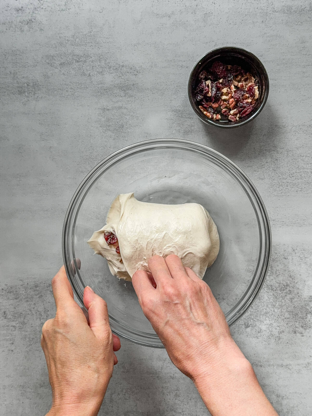 Dough with inclusions being folded by hand in a mixing bowl.