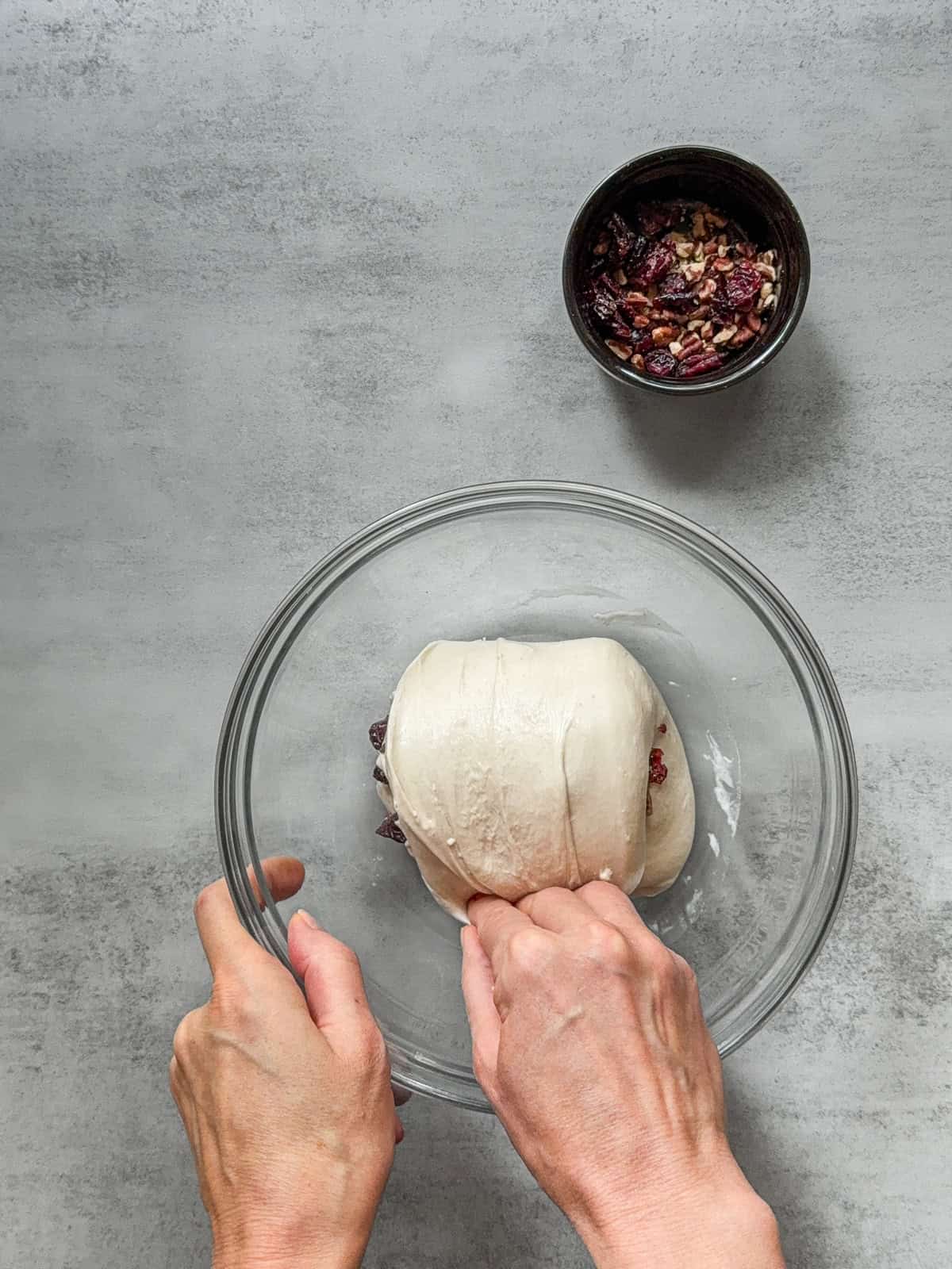 Dough with inclusions being folded by hand in a mixing bowl.