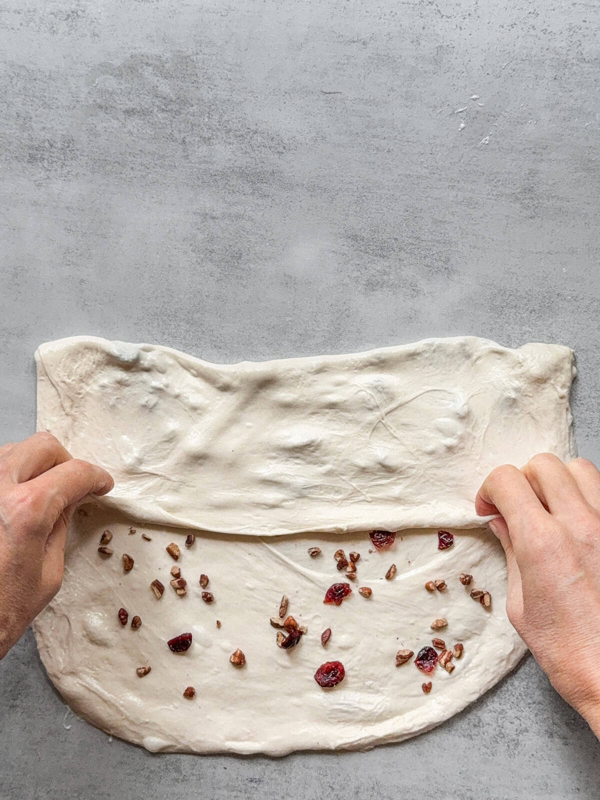 Hands folding the upper third of the dough with inclusions over the center.