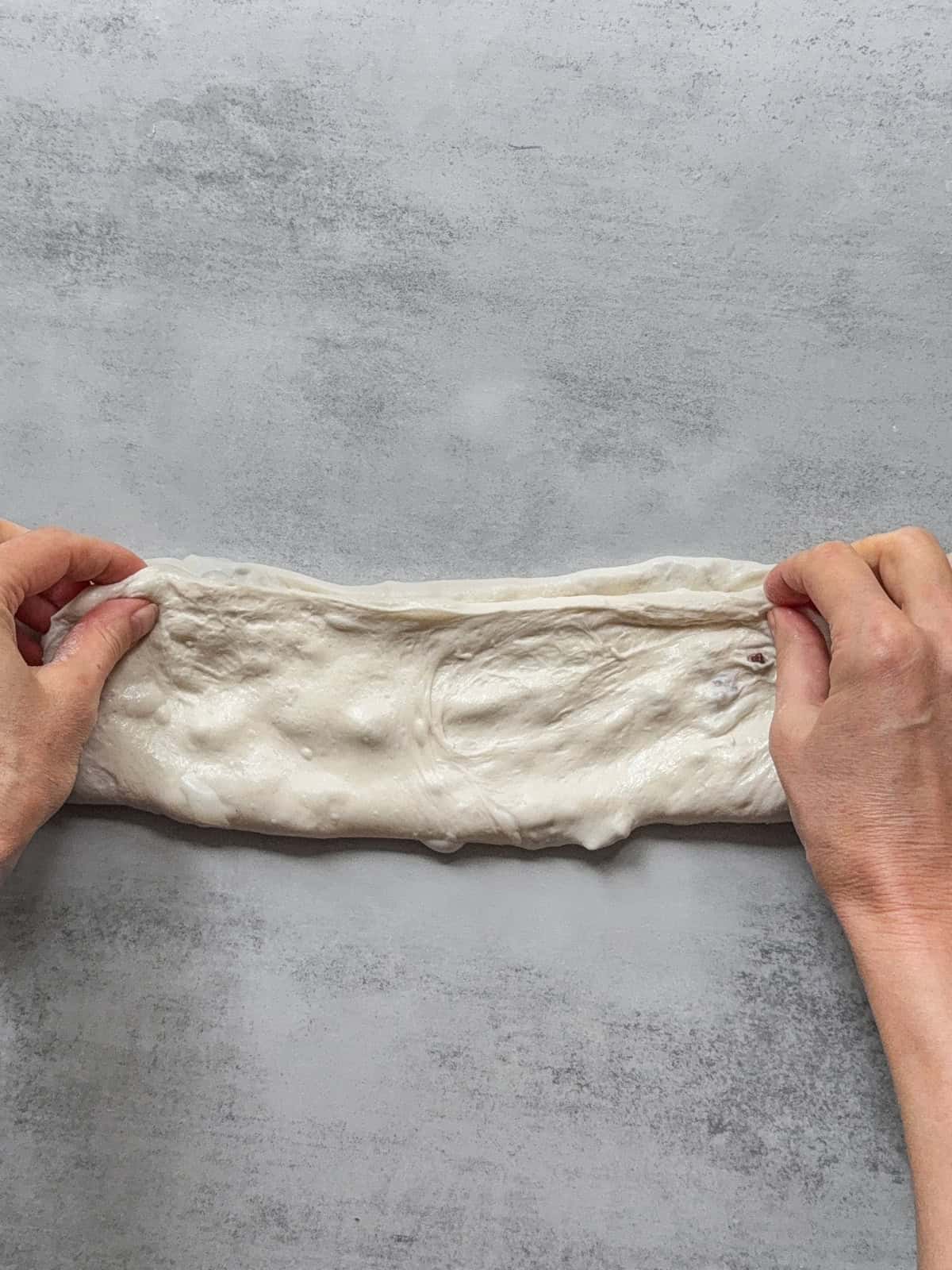 Hands folding the bottom third of the dough with inclusions over the upper third.