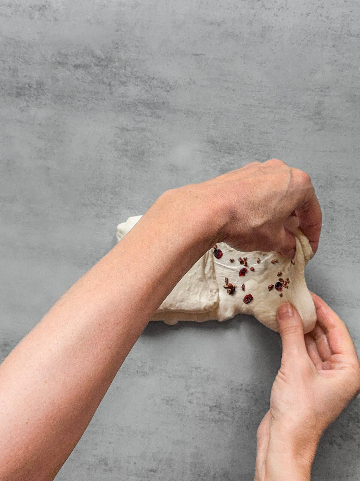 Hands holding the right third of the dough with inclusions.