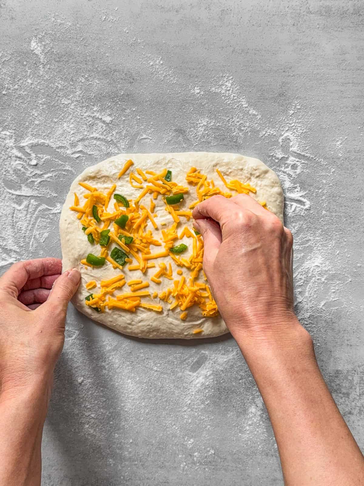 Hands sprinkling inclusions onto sourdough dough.