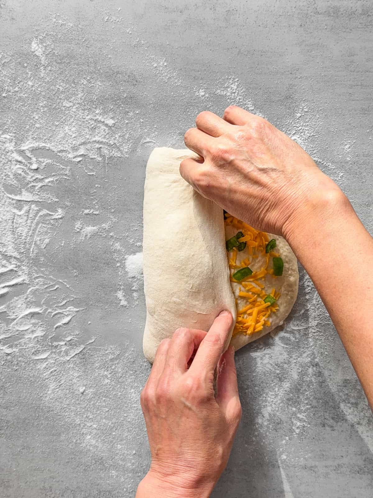Hands folding the left side of the dough to the center.