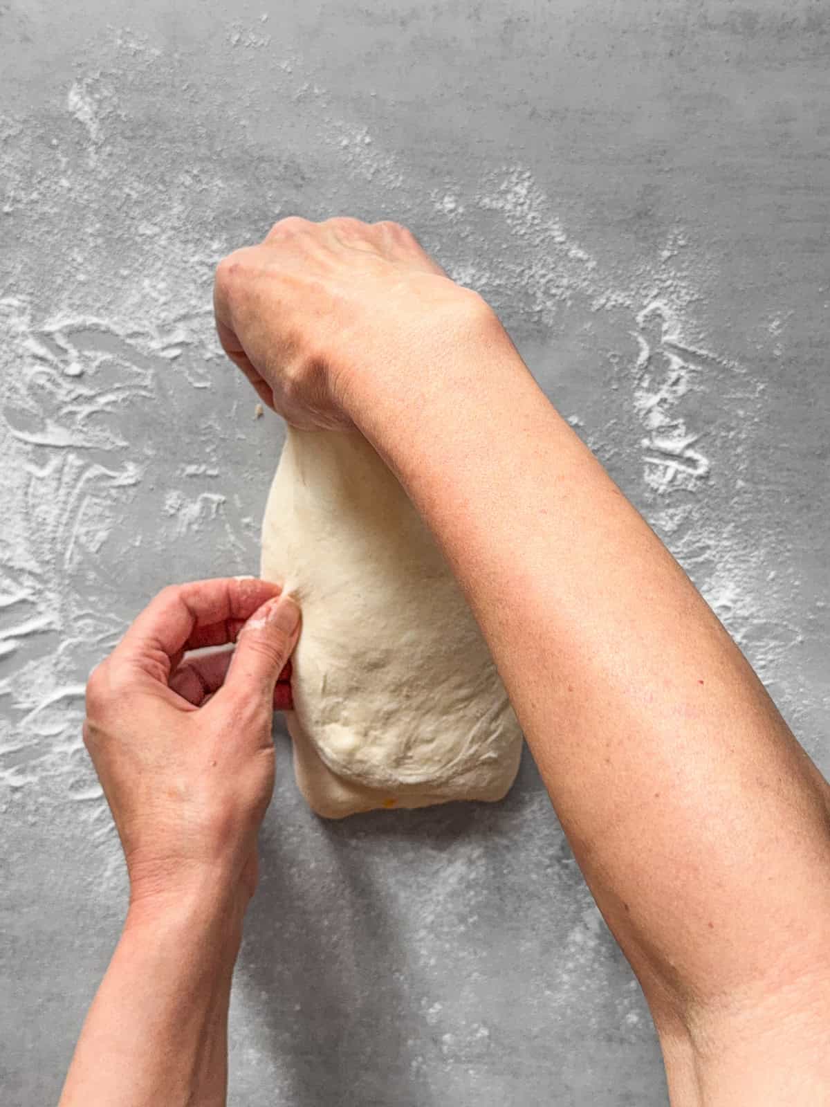 Hands overlapping the left side of the dough.
