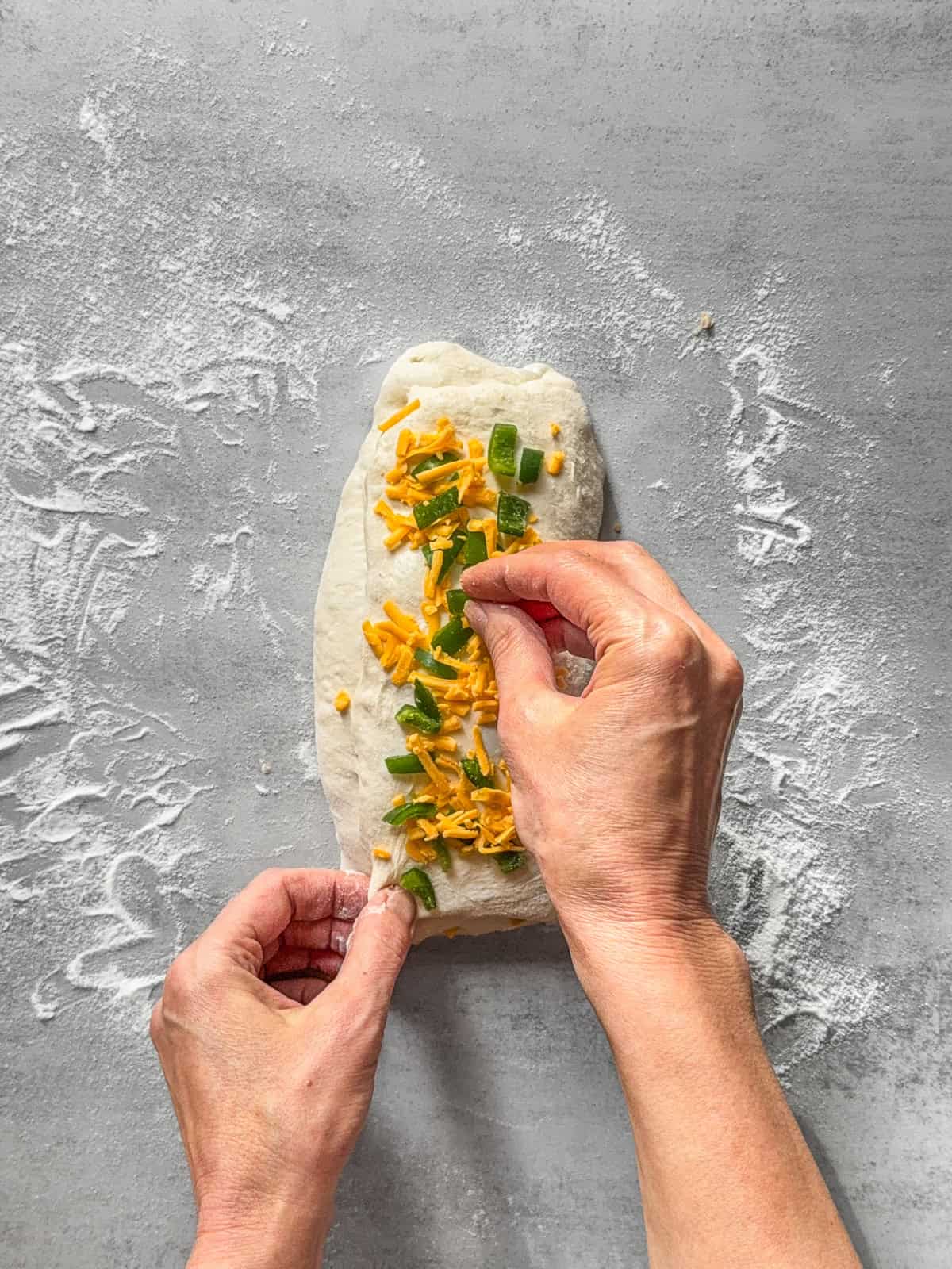 Hands sprinkling inclusions onto folded sourdough dough.