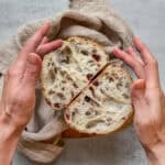Cranberry walnut sourdough bread, sliced in half, with hands around loaf.