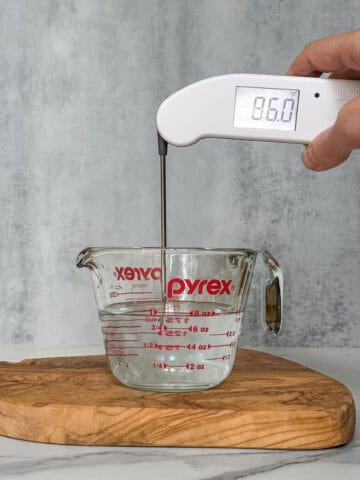 Hand holding a thermometer to measure water temperature for sourdough.