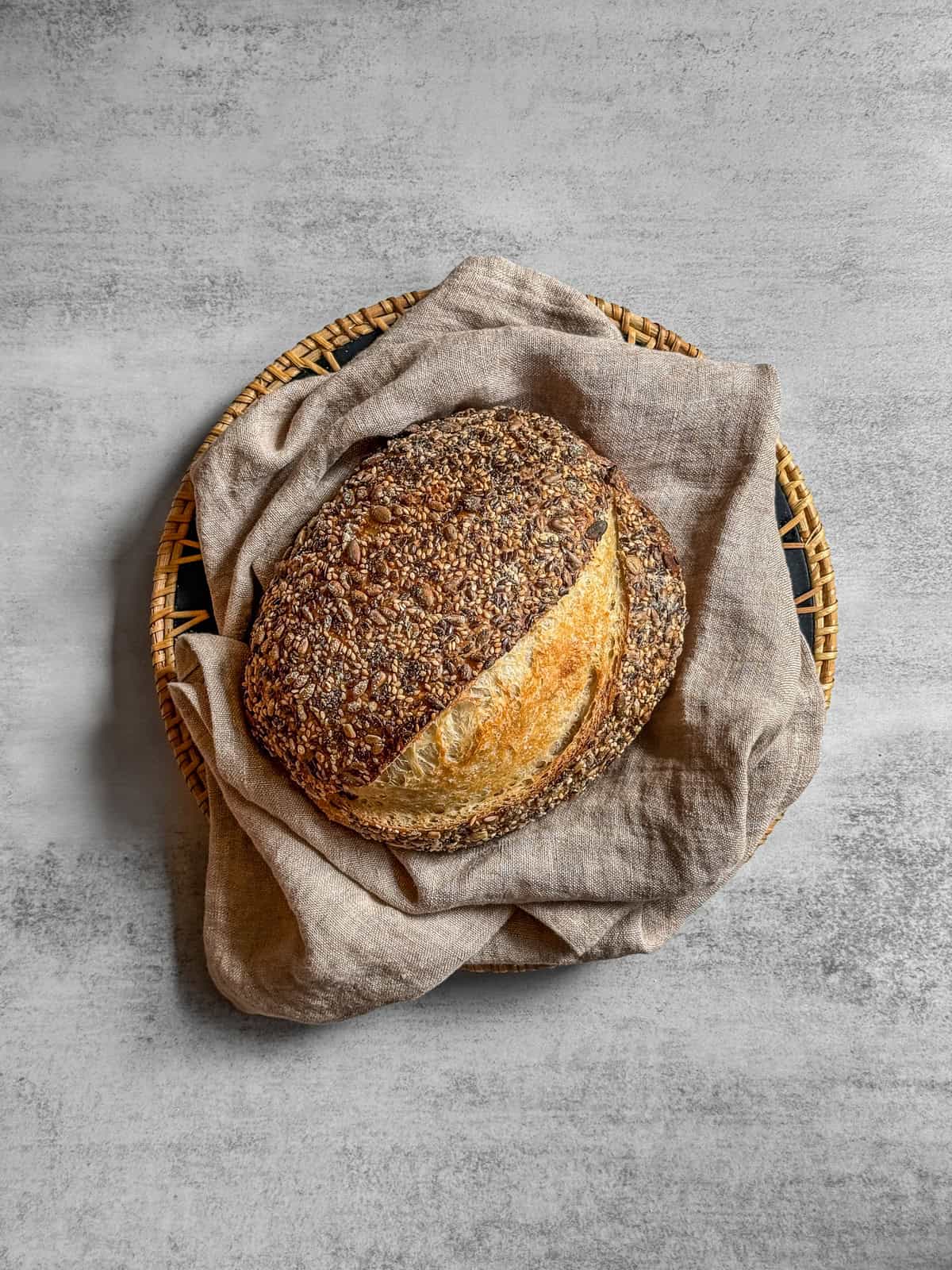 Sourdough bread topped with seeds in a bread basket lined with a towel.