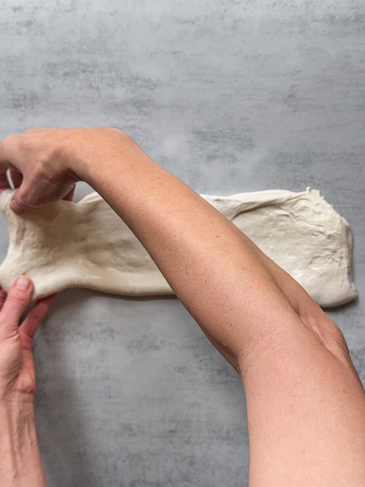 Hands holding the left third of the dough.