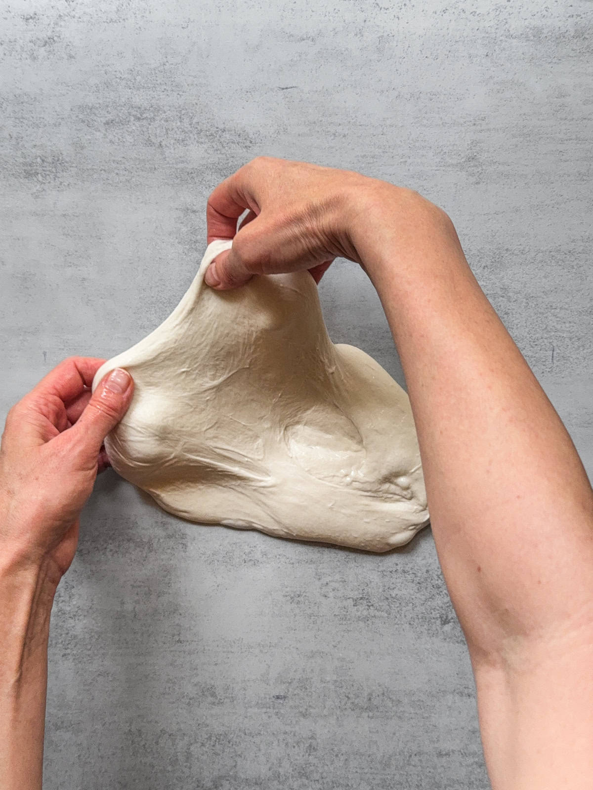 Hands stretching the dough away from the center.
