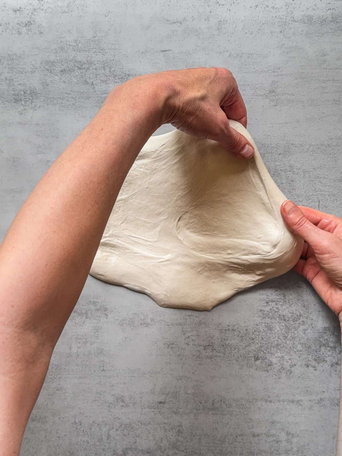 Hands stretching a corner of the dough.