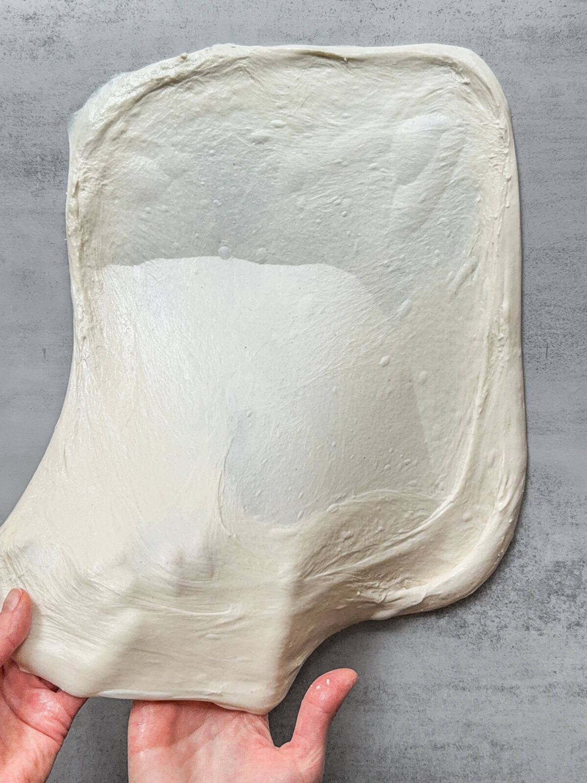 Hands stretching the dough into a thin rectangle.