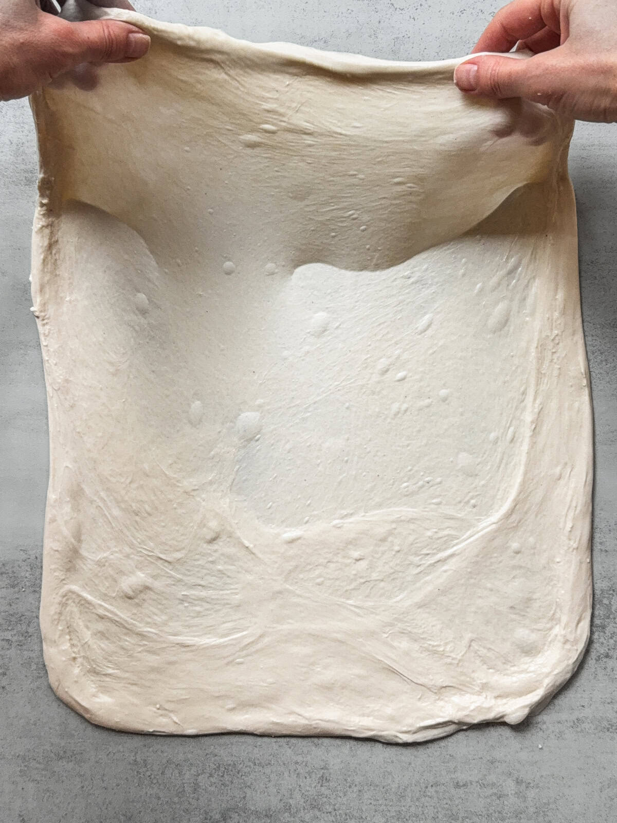 Hands holding the upper third of the dough.