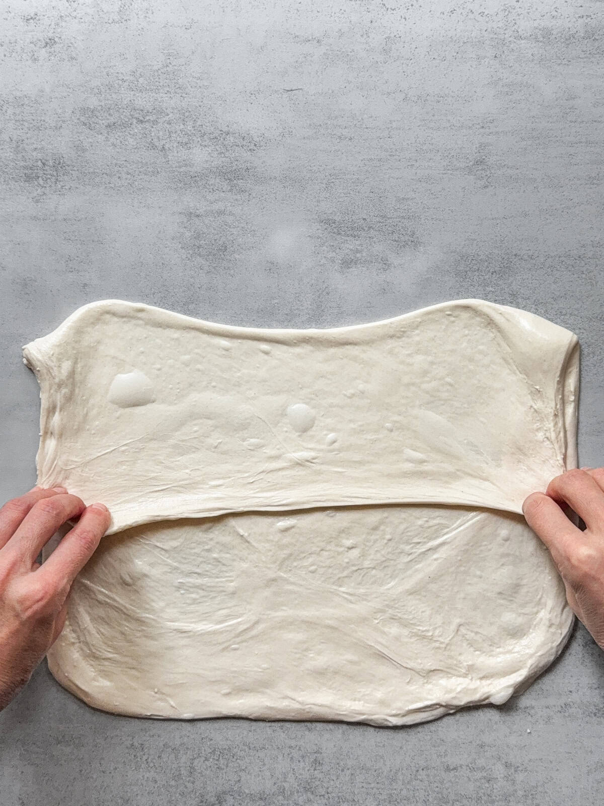 Hands folding the upper third of the dough over the center.