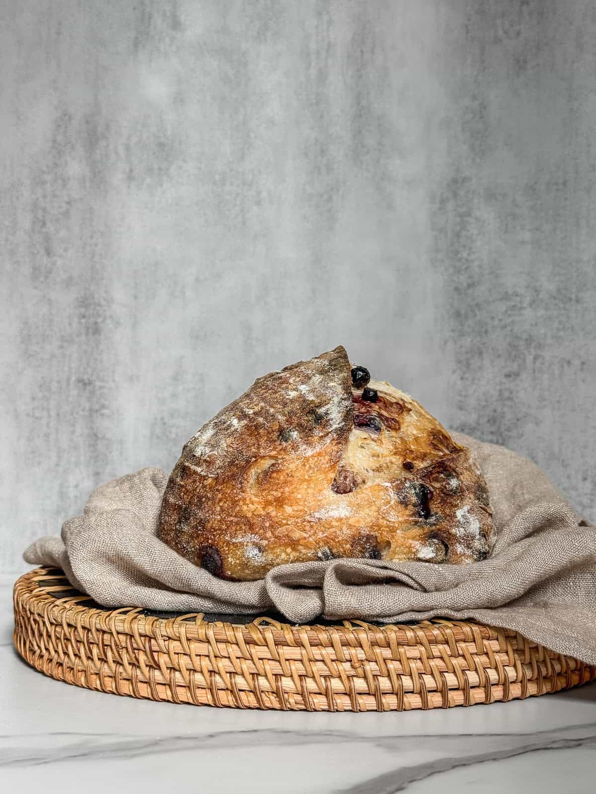 Loaf of lemon blueberry sourdough bread on a serving board lined with a kitchen towel.