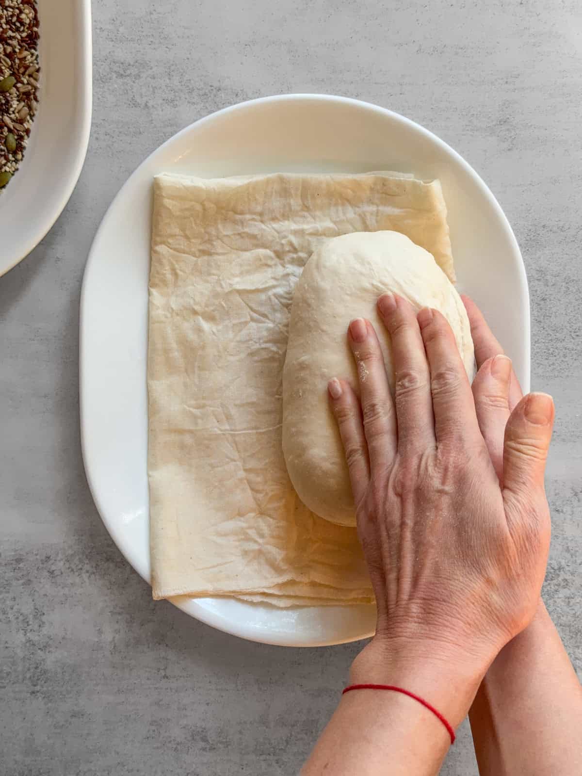 Hands rolling the dough to one side on a damp towel.