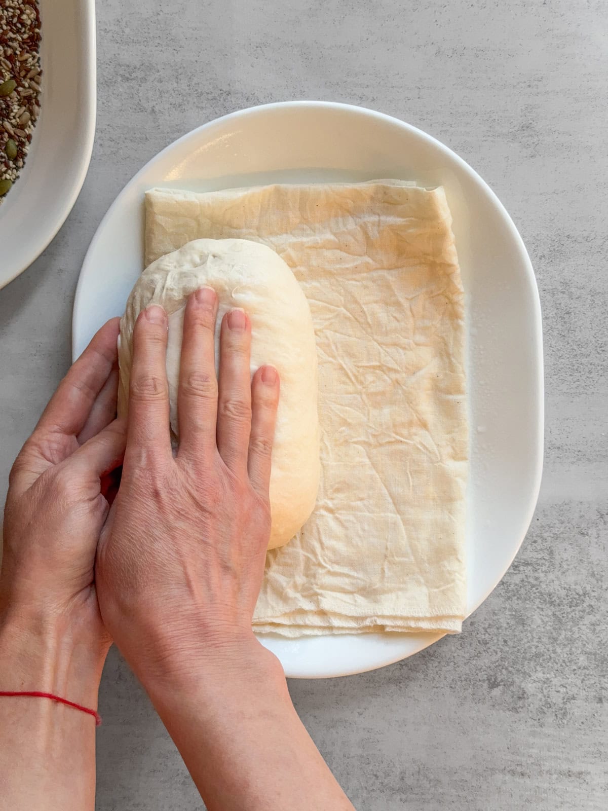 Hands rolling the dough to the other side on a damp towel.