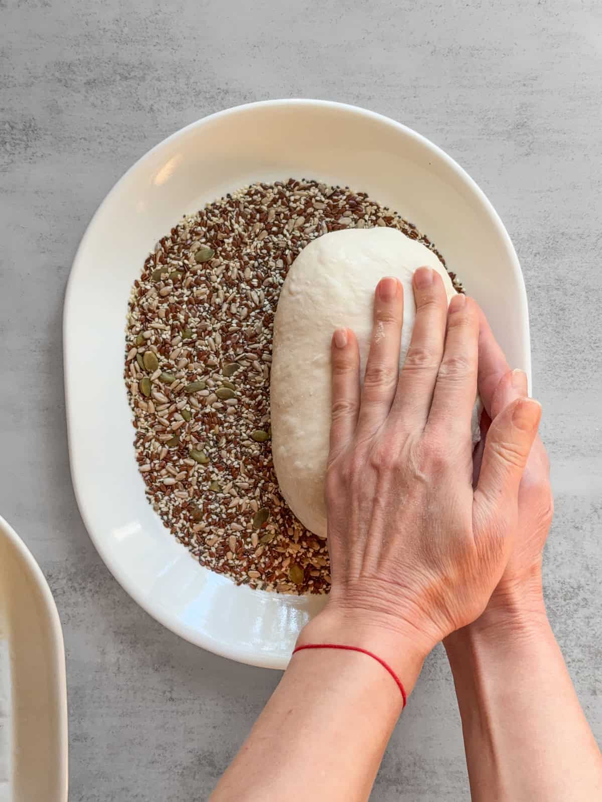 Hands rolling the dough over seeds on one side.