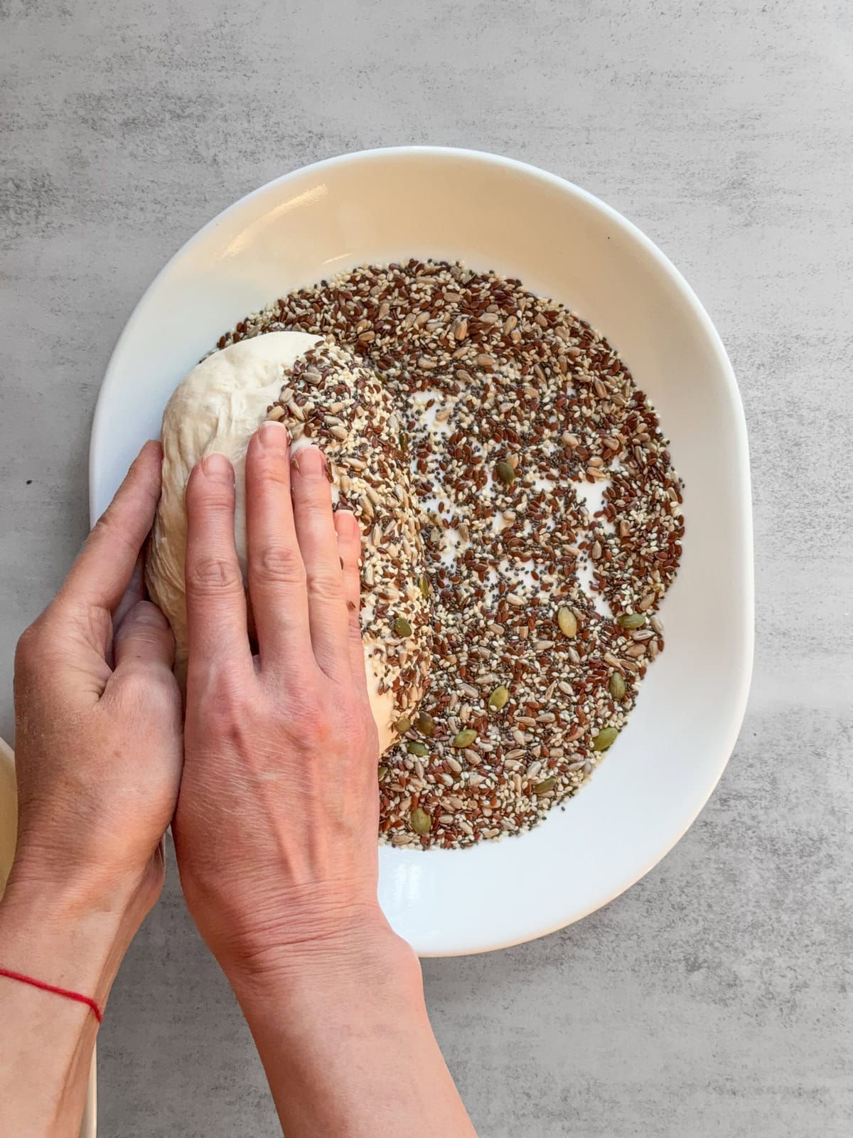 Hands rolling the dough over seeds on the other side.