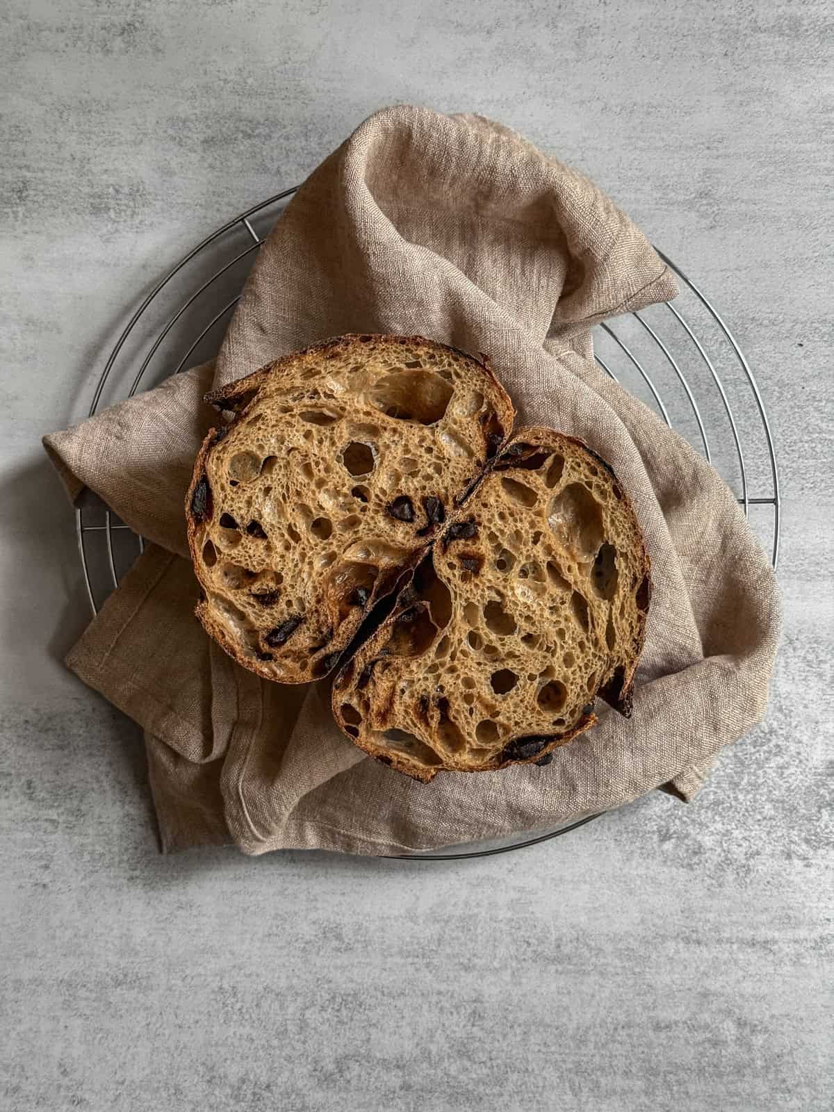 Halved black garlic sourdough bread loaf on a kitchen towel, showing crumb and texture.