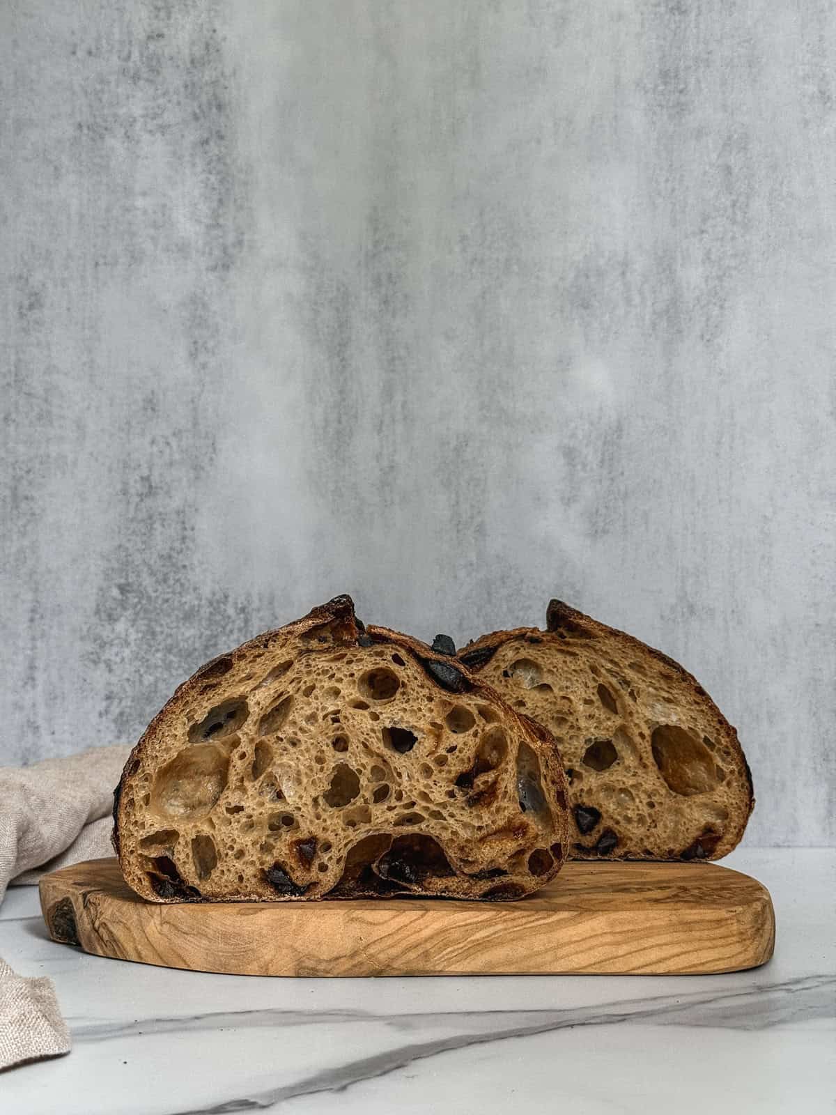 Two halves of black garlic sourdough bread on a wooden board, showing the crumb and texture.