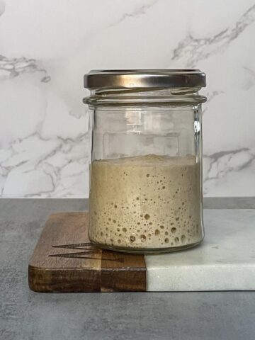 Jar of the overfed sourdough starter on a marble board.