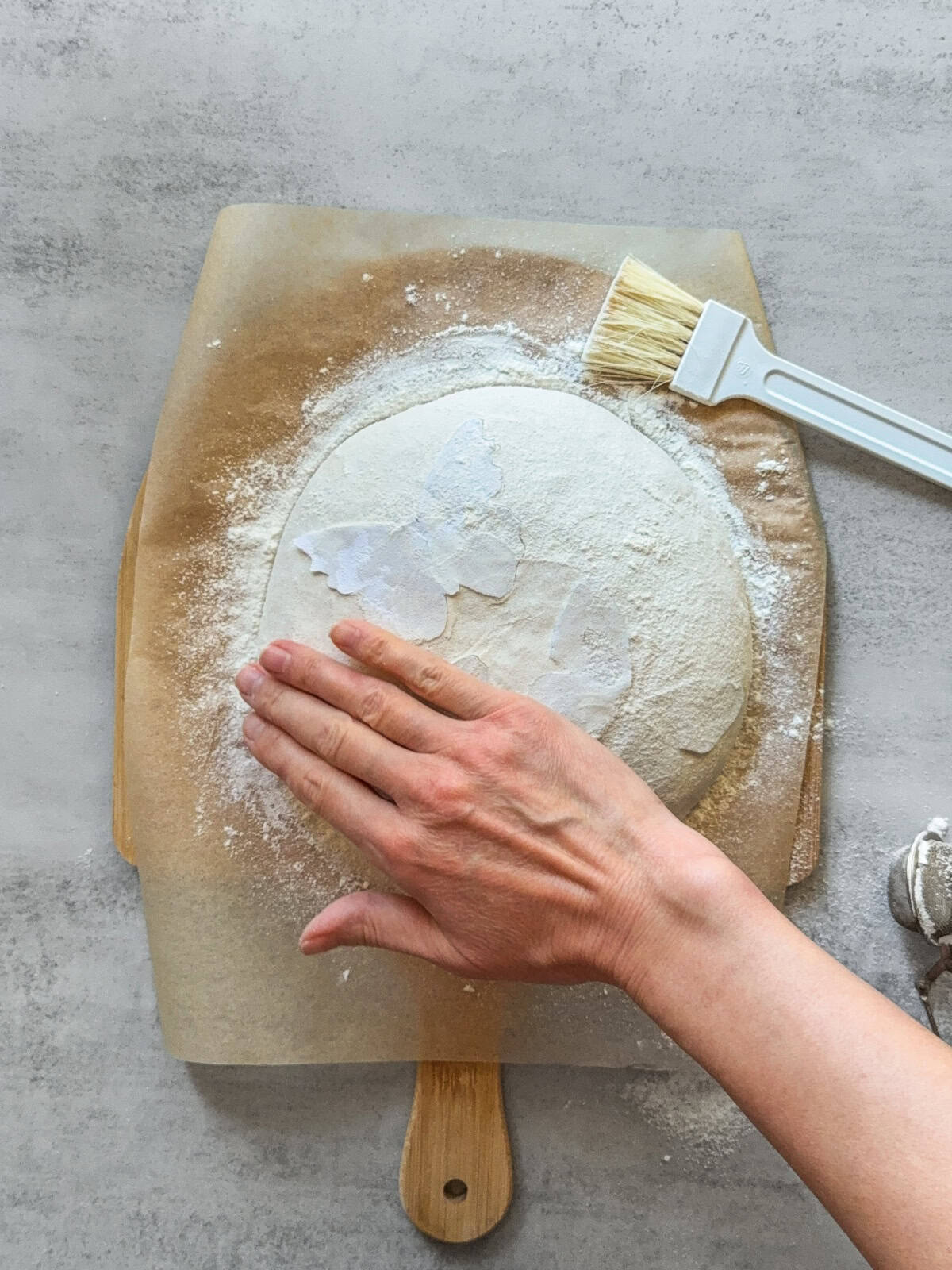 Hand spreading flour over the dough with a stencil in place.