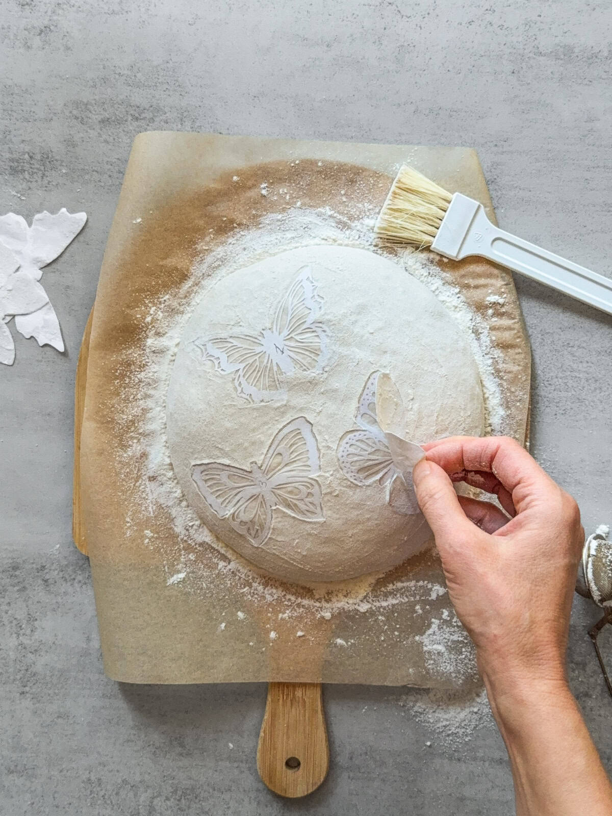 Hand removing the butterfly cutout from the dough surface.