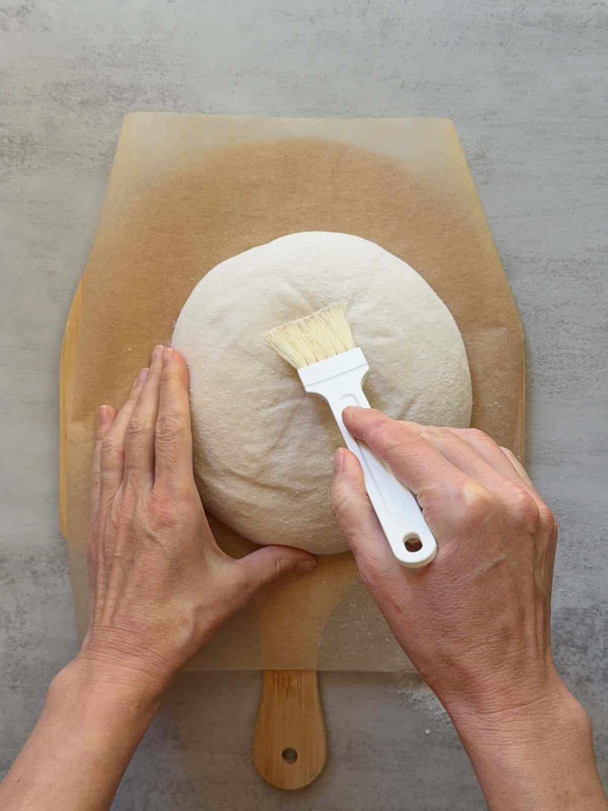 Hands brushing flour off the dough using a pastry brush.