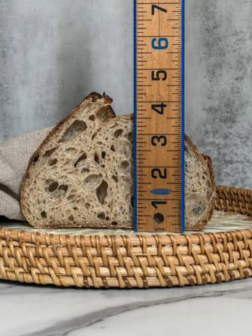 Half of a sourdough bread loaf with a wooden ruler measuring oven spring.