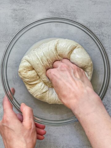 A hand folding sourdough dough toward the center in a bowl using the pinch and fold method.