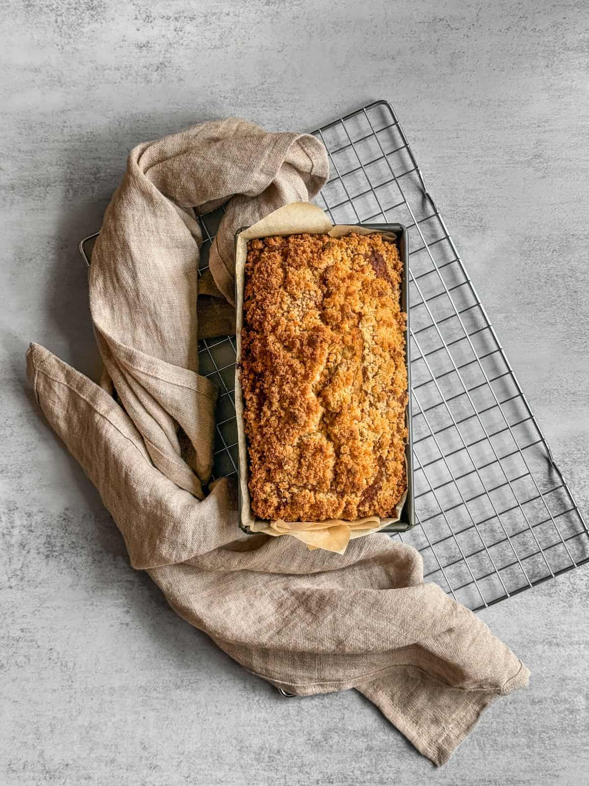 Sourdough discard banana bread in a loaf pan cooling on a wire rack with a kitchen towel nearby.