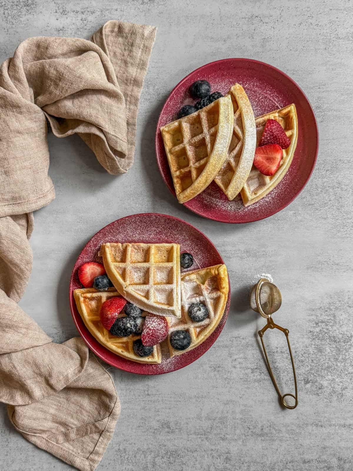 Sourdough waffles topped with fresh fruit and served on dessert plates, with a folded kitchen towel nearby.