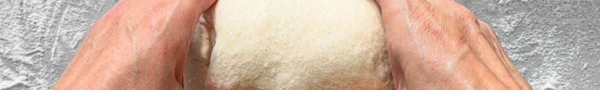 Hands shaping sourdough on a floured surface.